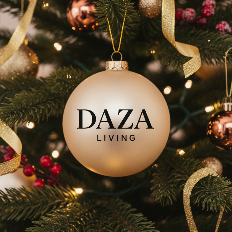 A gold Christmas bauble with the words DAZA LIVING hangs on a decorated tree with ribbons, berries, lights, and other ornaments in the background.