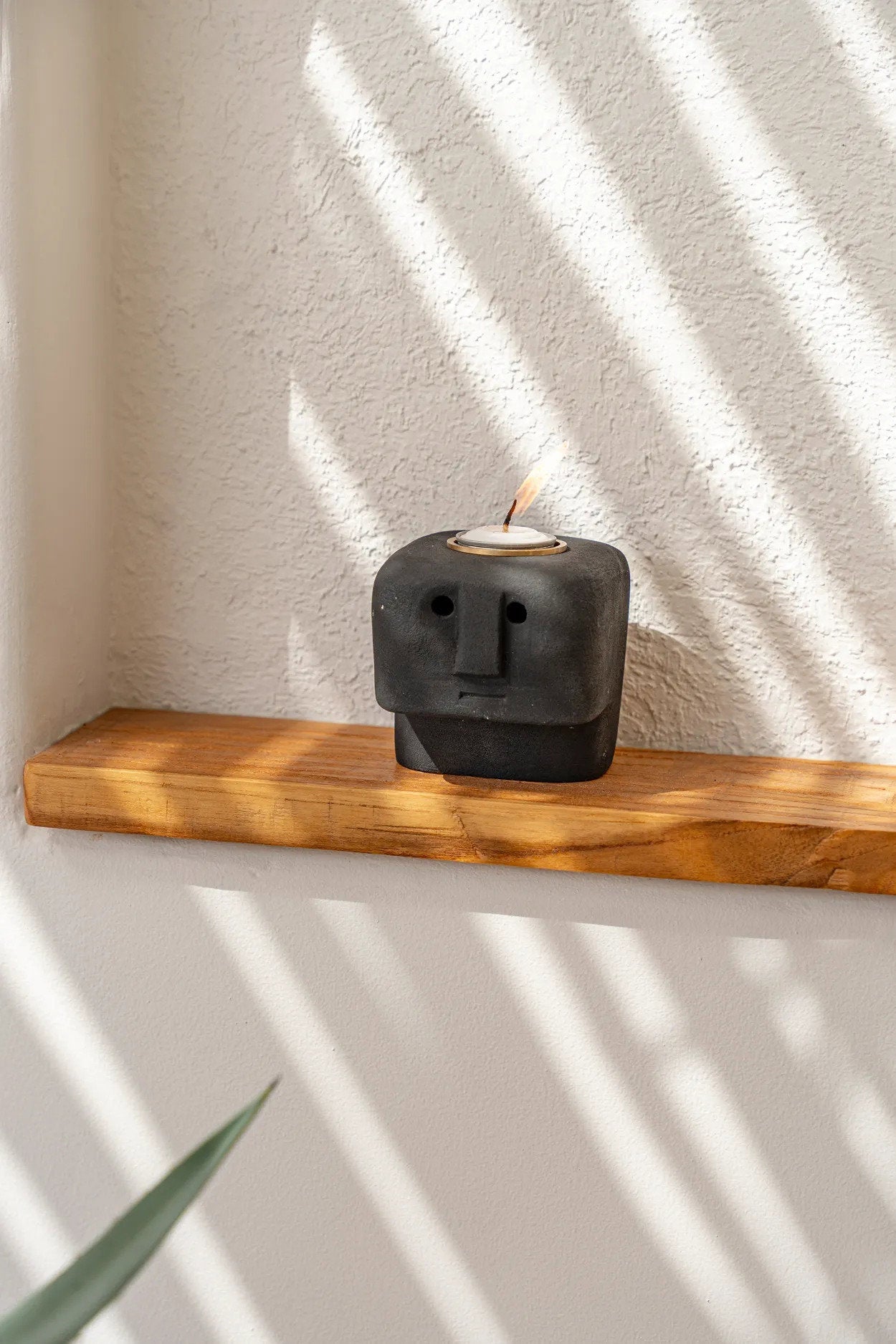 De Sumba Stone #26 kaarsenhouder, zwarte stenen figurine met gezicht, op houten plank